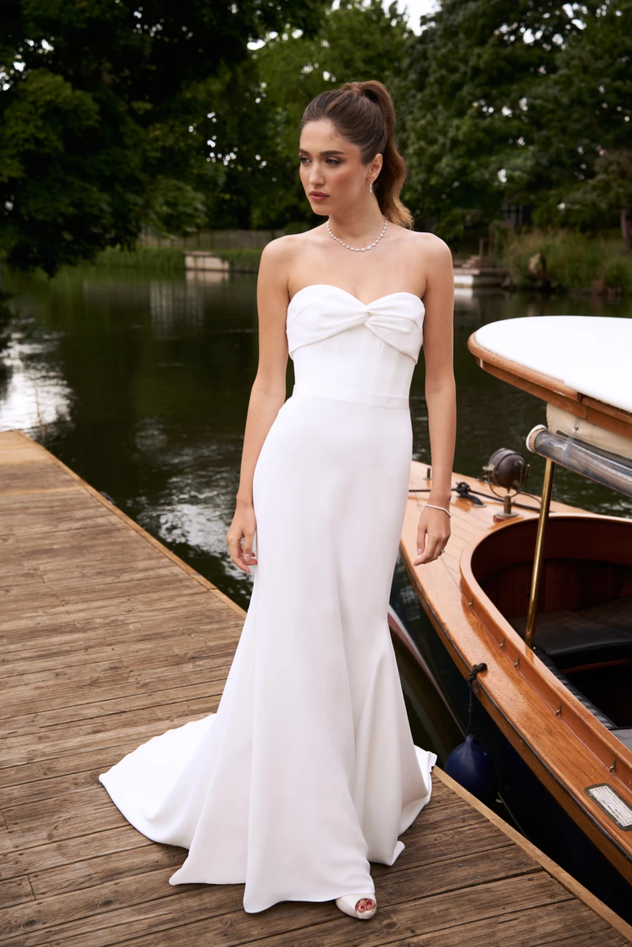 Model wearing a fitted wedding dress standing next to a lake